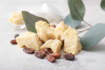 Pieces of cocoa butter and beans on light background