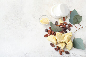 Pieces of cocoa butter, beans and jar of cream on light background
