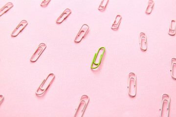 Green paper clip among pink ones on color background. Concept of uniqueness