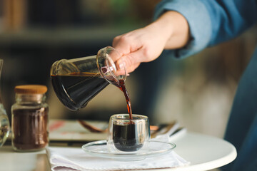 Woman pouring hot turkish coffee into glass cup at table, closeup