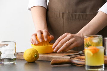 Woman squeezing orange for juice on table in kitchen