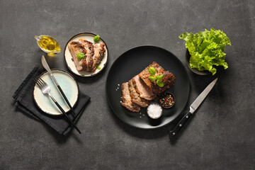 Plates with tasty beef brisket, lettuce and spices on dark background