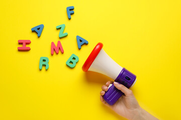 Woman with toy megaphone and letters on color background
