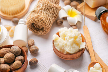 Bowl of shea butter, nuts and bath supplies on light background, closeup