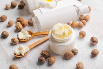 Fototapeta na wymiar Jar of shea butter, nuts and cosmetic products on light background, closeup