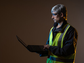 Portrait of a working engineer with a laptop. Working engineer in a yellow vest. A mature engineer is holding a computer. Сoncept - worker of an engineering company. Engineering bureau employee