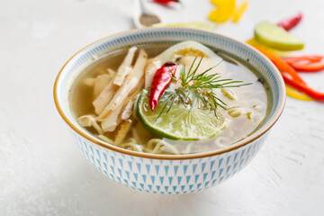 Bowl of tasty Thai soup with chicken on light background