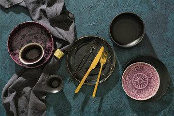 Different tableware, cutlery and napkin on dark background