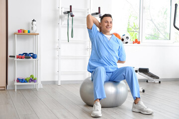 Fototapeta premium Male physiotherapist demonstrating exercise with fitball in rehabilitation center