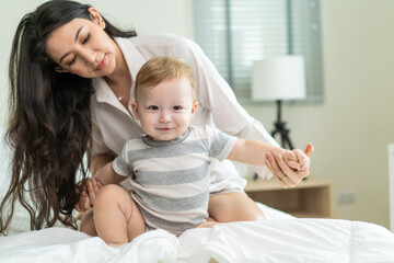 Fototapeta na wymiar Caucasian loving mom play with cute baby boy child on bed in bedroom.