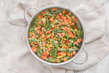 Colander with mix of frozen vegetables on light background, closeup