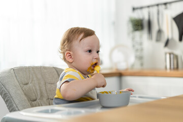 Caucasian young baby toddler eating healthy foods in kitchen at home.