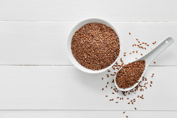 Bowl and spoon with flax seeds on light wooden background