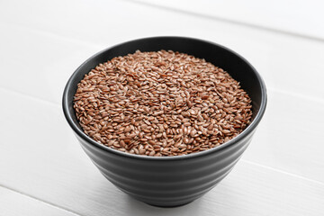Bowl with flax seeds on light wooden background, closeup