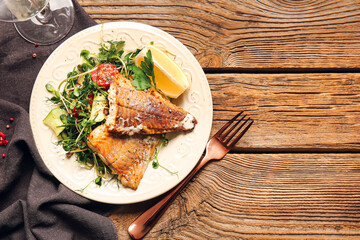 Plate with tasty baked cod fillet and vegetables on wooden background