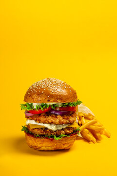 Fresh Big breaded chicken burger with double cutlet and fries on yellow background. Fat unhealthy street food. Copy space