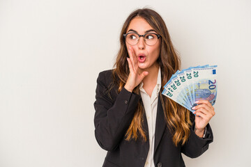 Young caucasian business woman holding banknotes isolated on white background is saying a secret hot braking news and looking aside