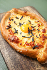 Wooden board with tasty Ajarian khachapuri on color wooden background, closeup