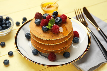 Plate of tasty pancakes with honey and berries on color wooden background