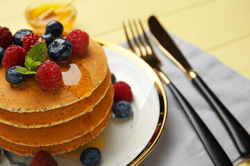 Plate of tasty pancakes with honey and berries on color wooden background, closeup