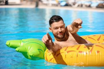 Young man with inflatable ring pointing at viewer in swimming pool