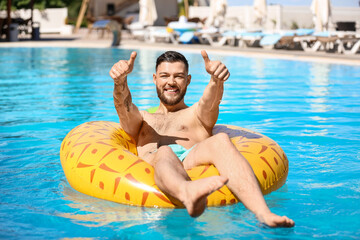 Young man with inflatable ring showing thumbs-up in swimming pool