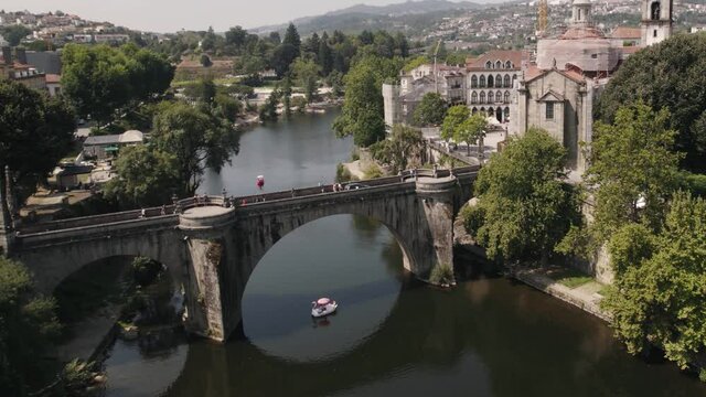 Swan boat sailing under historical castle bridge in Amarante town, Portugal. Aerial ascend view