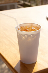 Close up of takeaway blank white disposable cup and tube of cold soft drink on wooden table. The sunlight shines in the back. summertime.