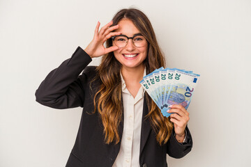 Young caucasian business woman holding banknotes isolated on white background excited keeping ok gesture on eye.