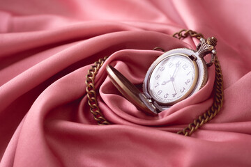 The vintage watch necklace is placed on the pink gold fabric