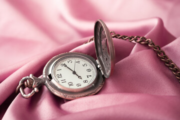 The vintage watch necklace is placed on the pink gold fabric.