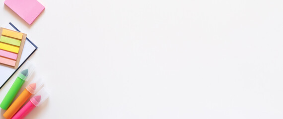 Banner with markers, stickers and notepad on a light white background. Colored office school supplies on the left side. Flatlay with copy space.