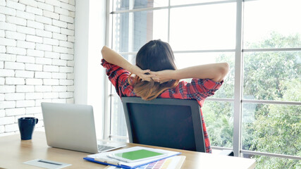 Woman streching arm raised sitting incorrect position home office desk. Back side of young asian...
