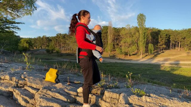 Woman with a baby in a sling ergo backpack traveling outdoor, family vacations adventure, mom with baby boy in infant kid carrier hiking. High quality 4k footage