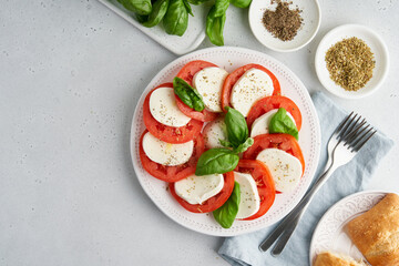 Horizontal flat lay of classic talian caprese salad with sliced tomatoes, mozzarella, basil, olive oil, pepper, salt and toast. Rustic mediterranean meal on light background. Copy space
