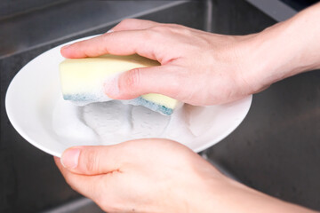 The young man's hands were cleaning dishes and bowls in the sink, and he used a sponge and foam to clean dirt and grease from food.