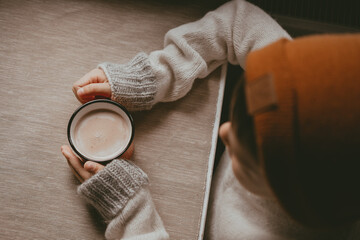 hands in a sweater hold hot cocoa, in a red mug, top view. A cozy photo with a mug in hand with copy space. Child drinks hot chocolate