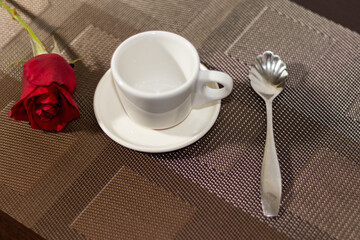 taza de porcelana color blanca  con decoración de rosa roja en mantel cafe y cuchara