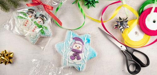 banner with packing of Christmas gingerbread cookies with snowmen on a gray background with fir branches, scissors, colorful ribbons, bows. soft focus. top view