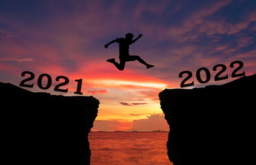 A young man jump between 2021 and 2022 years over the twilight sky and through on the gap of hill ...