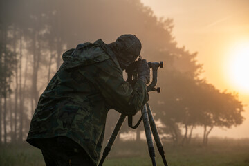 Nature photographer standing in camouflage clothing with a camera on a tripod