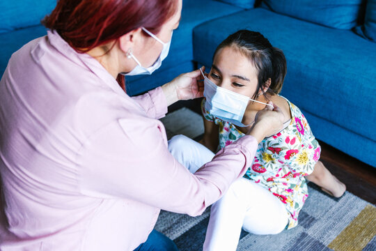 Latin Mother Wearing Face Mask On Her Daughter With Cerebral Palsy At Home In Latin America In Disability Concept During Covid Coronavirus Pandemic