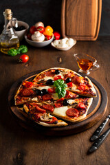 Fresh homemade italian pizzas with mozzarella, pepperoni sausages, olives and basil on the wooden table vertical photo