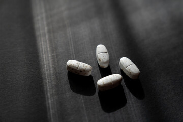 White spoiled pills covered with mold. Pills on a black background. The expiration date has expired. Light comes from a window