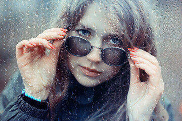 seasonal autumn pornetret, sad girl behind wet glass, raindrops background
