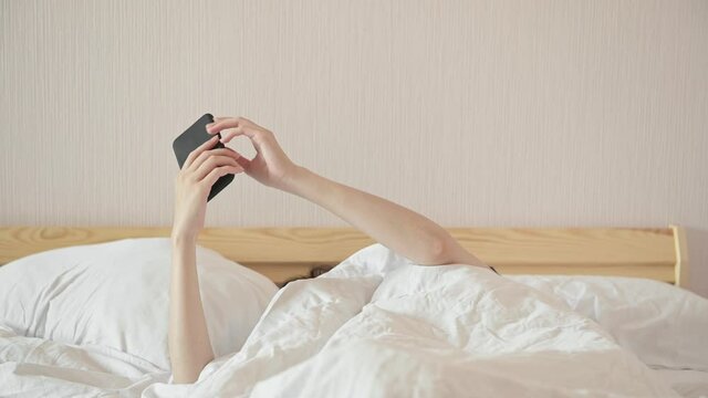 Woman checks news websites on cellphone lying in large double comfortable bed in light room close view. Internet addiction problem