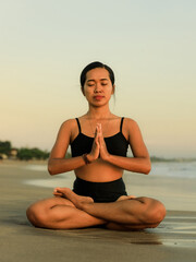 Fototapeta na wymiar Yoga retreat. Asian woman practicing Lotus pose. Padmasana. Hands in namaste mudra. Closed eyes. Healthy lifestyle. Yoga on the beach. Copy space. Seminyak beach, Bali
