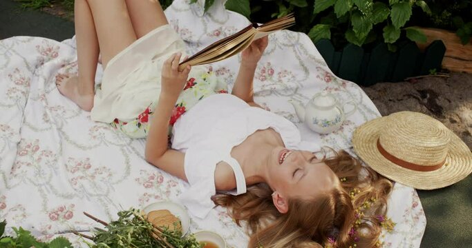 Cheerful young girl lying and reading book in garden. High angle view of adorable teenage girl laughing while reading book outdoors at summertime