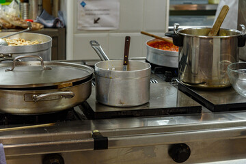 casseroles on the fires of a restaurant. You can see casseroles of different shapes, with wooden ladles and spoons, two more casseroles with cominda on the left, another with a lid on the left. Food i