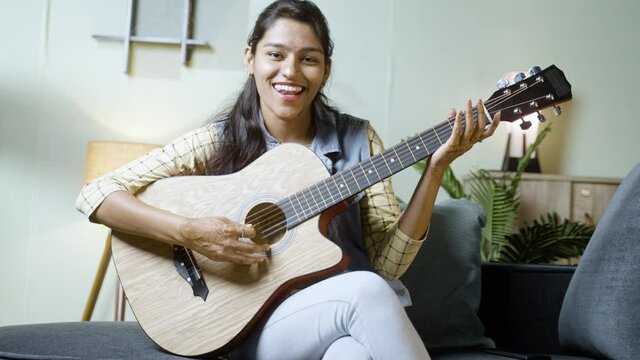 Happy smiling young Inidan girl playing acoustic guitar by looking at camera